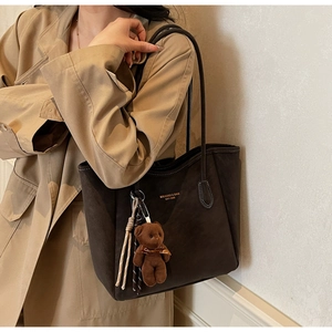 Detail of dark brown tote bag with gold stitching, brand logo, and plush bear charm