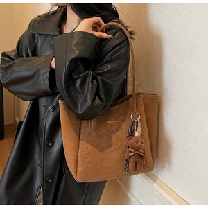 Detail of brown suede tote bag with golden logo and plush bear charm on model shoulder