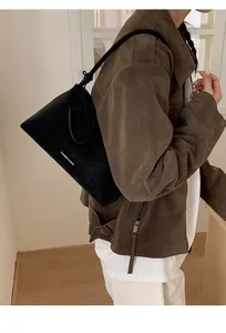 Detail of black suede shoulder bag with thin straps worn by a model in soft lighting