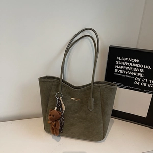 Macro view of olive green suede tote bag showing gold logo and plush bear charm