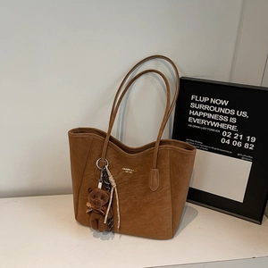 Detail of a brown leather tote bag with gold logo text and a plush bear charm decoration