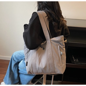 Detail of grey canvas tote bag with wide shoulder strap and brand label on side