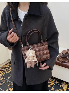Détail d'un sac bandoulière à carreaux marron avec charme ours sur manteau gris