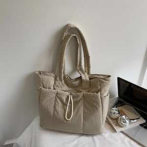 Close-up of quilted beige tote bag featuring elastic drawstring pocket and side compartments