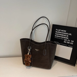 Close-up of brown faux leather tote bag texture with brand logo and cute bear charm