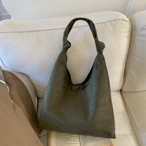 Detail of dark green suede tote bag with stylish knot strap on white fabric sofa