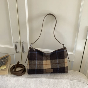 Detailed macro view of the retro checkered fabric and brown leather strap on a tote bag