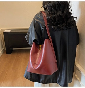 Close-up of vintage burgundy bucket bag with gold buckle on black leather coat