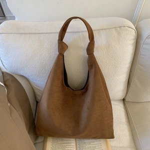 Detail of dark brown suede hobo bag with unique knot shoulder strap on a cozy sofa