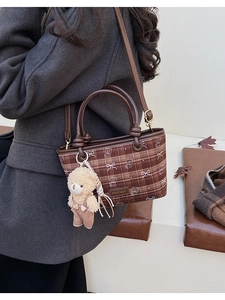 Détail du sac à carreaux avec breloque ours et motif nœud sur tissu marron élégant