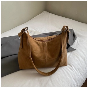 Detail of a brown suede tote bag with cross stitching and vintage silver metal buckles