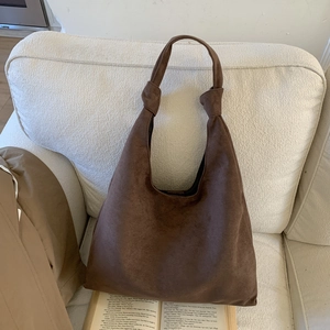 Detail of dark brown suede tote bag with knotted shoulder strap on a cozy white sofa