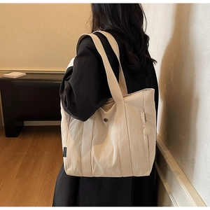 Detail view of the beige canvas tote bag with a black label on model back