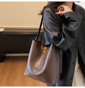 Brown faux leather bucket bag with gold hardware worn by a model in a warm indoor setting