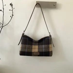 Detailed view of checkered wool tote bag with leather strap and fashion label on a white wall