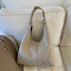 Detail of minimalist beige suede tote bag with stylish knot strap on a soft fabric sofa