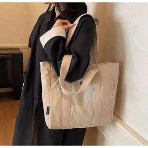 Detail view of a beige high-capacity canvas tote bag with black woven brand label