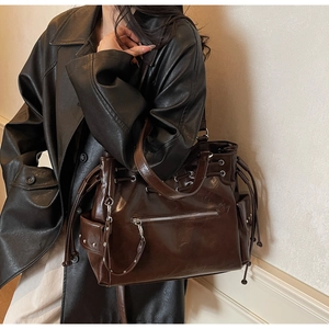 Detailopname van donkerbruine glanzende tote bag met trekkoord en metalen klinknagels