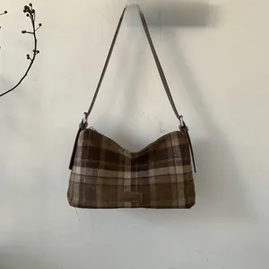 Close-up of the vintage brown plaid fabric and leather brand tag on this tote bag