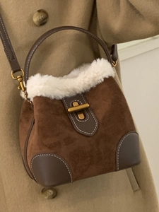 Sac seau en daim marron et peluche blanche avec détails dorés porté sur un manteau