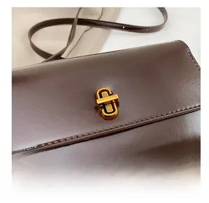 Gros plan du fermoir rotatif doré sur le sac à bandoulière en cuir marron foncé