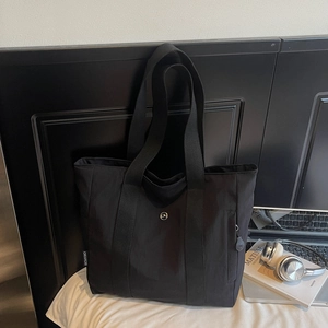 Detail shot of black canvas tote bag showing the side brand label and metal buckle fastener