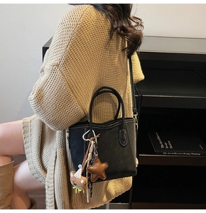 Detail der schwarzen Ledertasche mit weißen Kontrastnähten und süßem Bärenanhänger