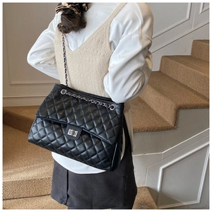 Détail d'un sac cabas noir matelassé avec bandoulière chaîne argentée porté par une femme