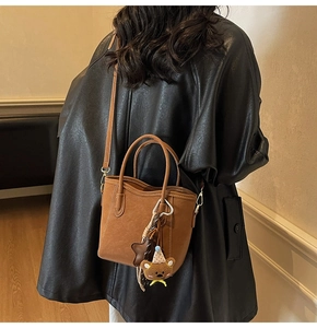 Braune Shopper-Tasche aus Kunstleder mit Schultergurt und Bärenanhänger am Modell
