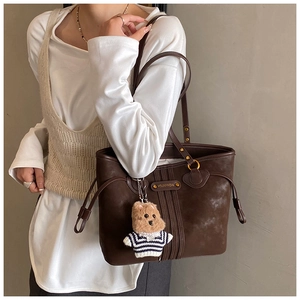 Détail du sac cabas marron vintage avec plaque logo dorée et charm d'ours en peluche