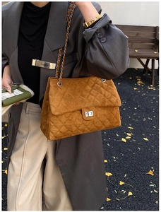 Gros plan du sac bandoulière en daim marron matelassé avec chaîne et fermoir rotatif