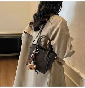 Detail der dunkelbraunen Eimer-Tasche aus Leder mit weißen Nähten und Bärenanhänger