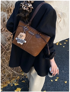 Détail d'un sac cabas en daim marron avec pendentif ours dans un décor d'automne extérieur