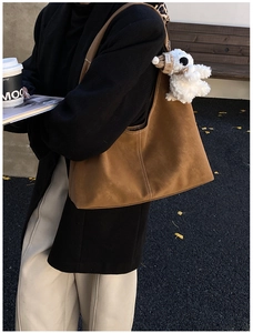 Detail view of brown suede shoulder bag with contrast stitching and cute plush dog charm