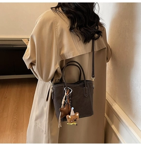 Detailaufnahme der dunkelbraunen Eimertasche mit Kontrastnähten und süßem Bärenanhänger