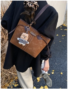 Détail d'un sac cabas marron foncé en daim avec anses en cuir et petit ours en peluche