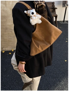 Detail of a large brown suede tote bag featuring a cute teddy bear charm with Lovely tag