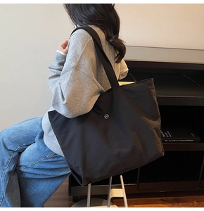 Détail d'un grand sac cabas noir avec logo métallique CM porté à l'épaule