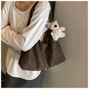 Detail of dark brown tote bag featuring white contrast stitching and a cute plush bear charm