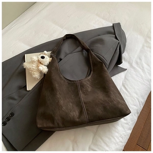 Detail of dark brown hobo bag with contrast stitching and plush bear charm on a grey suit