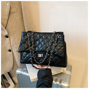 Détail du sac matelassé noir avec chaîne et fermoir rotatif argenté sur valise