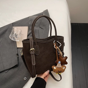 Detail der dunkelbraunen Wildleder-Beuteltasche mit Ziernaht und Bärenanhänger auf Sakko