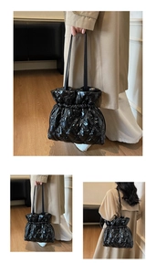 Detail showing shiny quilted texture and drawstring closure of the black padded tote bag