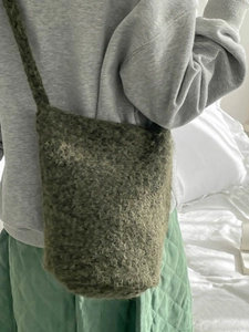Sac seau en sherpa vert foncé à texture pelucheuse et bandoulière porté sur un sweat