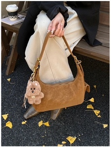 Detailed view of brown suede hobo bag with a cute plush bear charm on a park bench