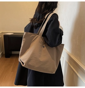 Vue latérale d'un grand sac cabas kaki minimaliste avec bouton métallique porté à l'épaule