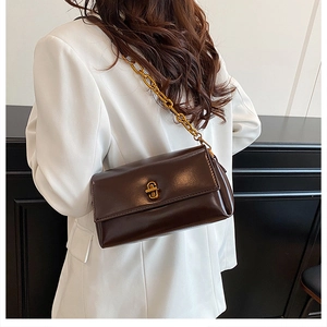 Détail du sac bandoulière en cuir brillant marron foncé avec chaîne dorée et boucle