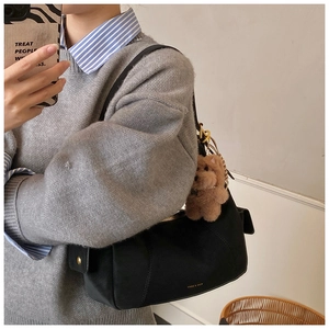 Detail of a black suede shoulder bag with a teddy bear charm for daily fashion