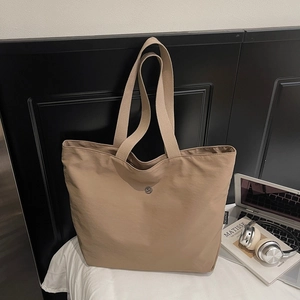 Gros plan du sac cabas en nylon kaki avec bandoulière large et logo sur fond de cuir noir