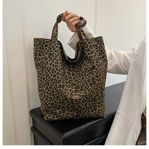 Detailed close-up of leopard print canvas tote bag with metal logo on a black locker